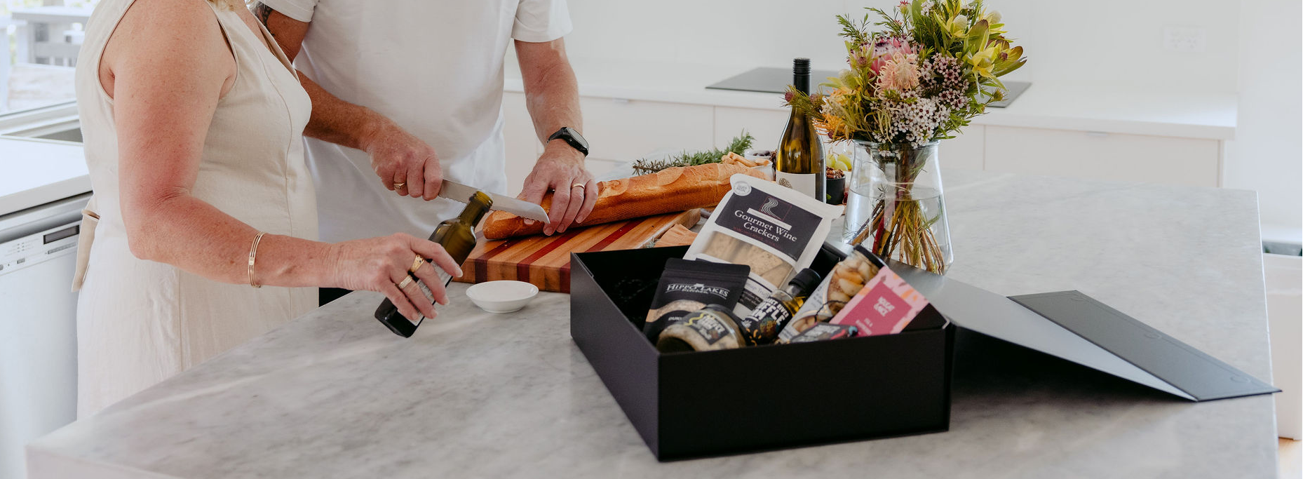 Man and woman in a kitchen opening a box of food items.